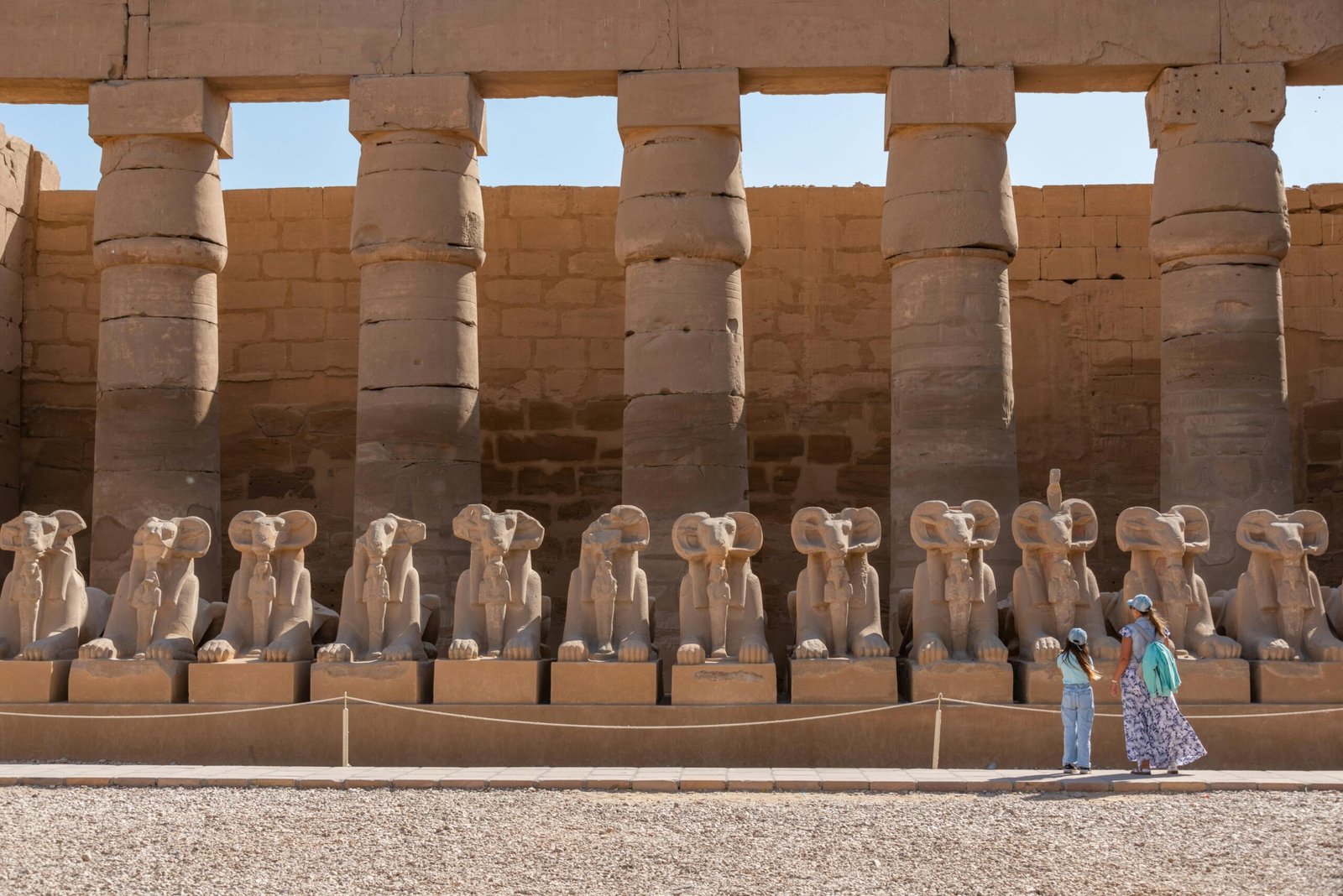 A view of the ram-headed sphinx statues at Karnak Temple Complex with visitors exploring the site.