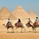 Tourists riding camels near the Great Pyramids of Giza, Egypt under clear skies.